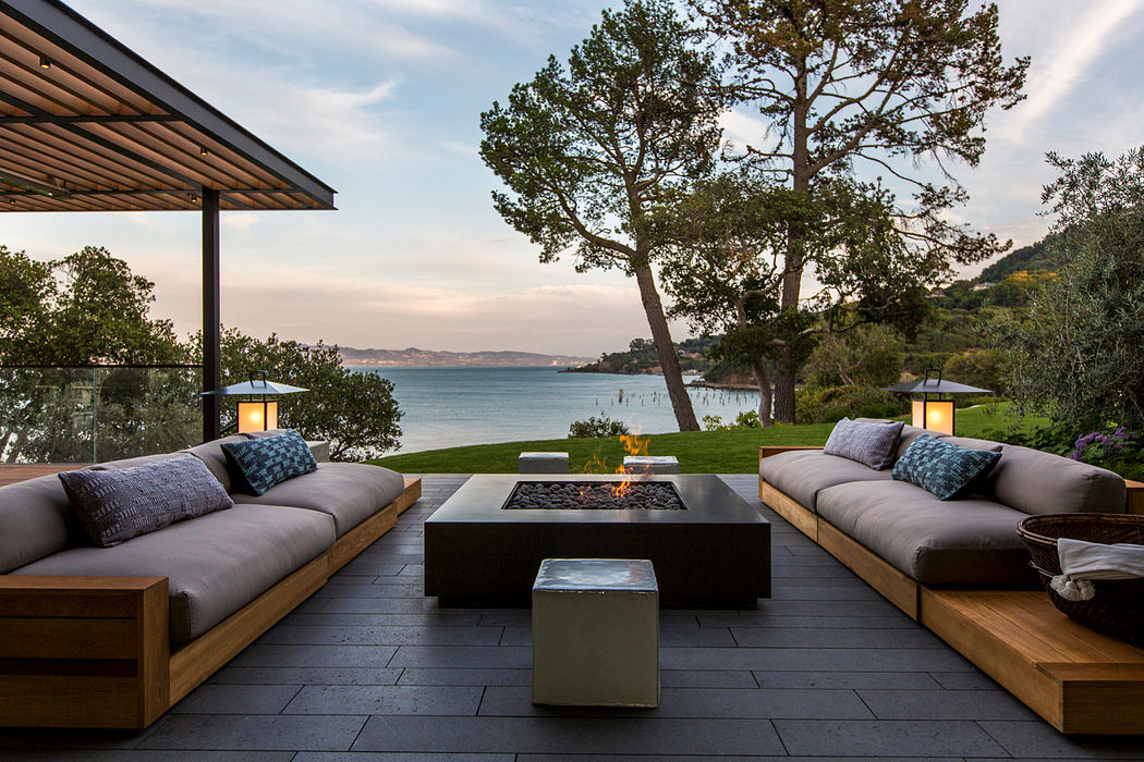 Outdoor living space with wood and stone furniture, fire pit, and scenic waterfront view.