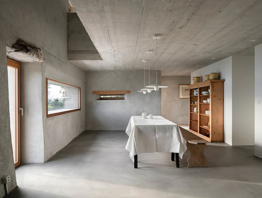 Minimalist dining room with concrete walls, wooden furnishings, and pendant lights.