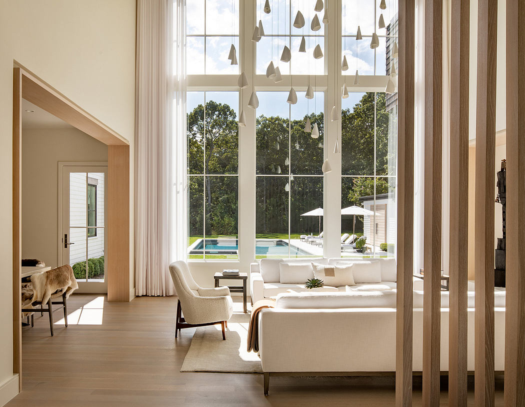 Bright, airy living space with large windows overlooking a lush outdoor pool area. Modern, minimalist decor.