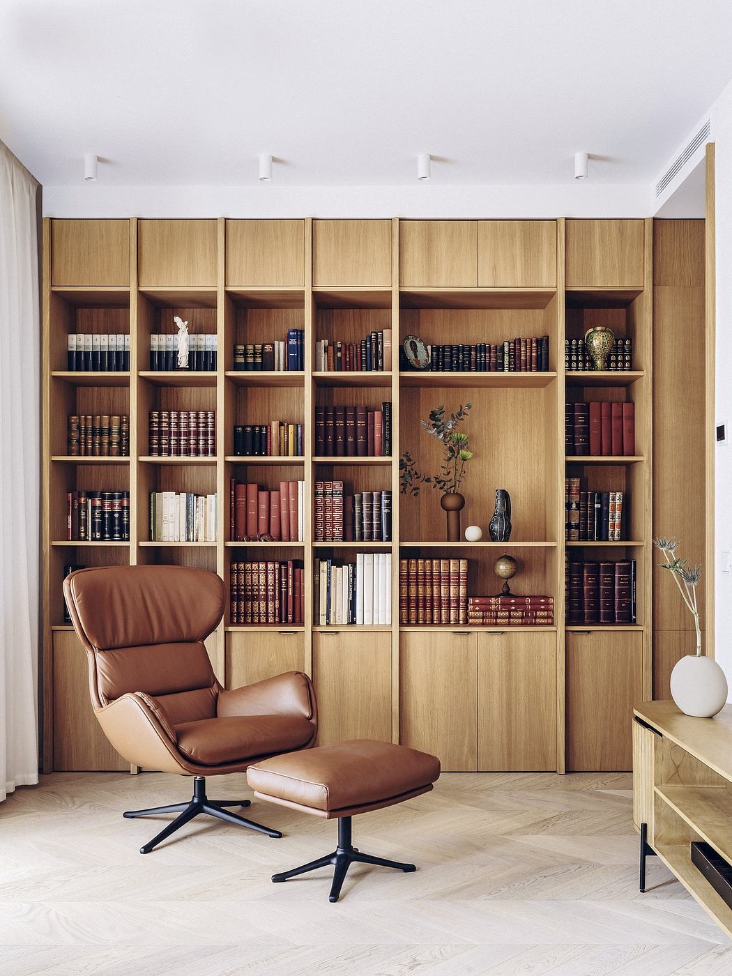 A cozy reading nook with a large wooden bookshelf, comfortable leather chair, and minimal decor.