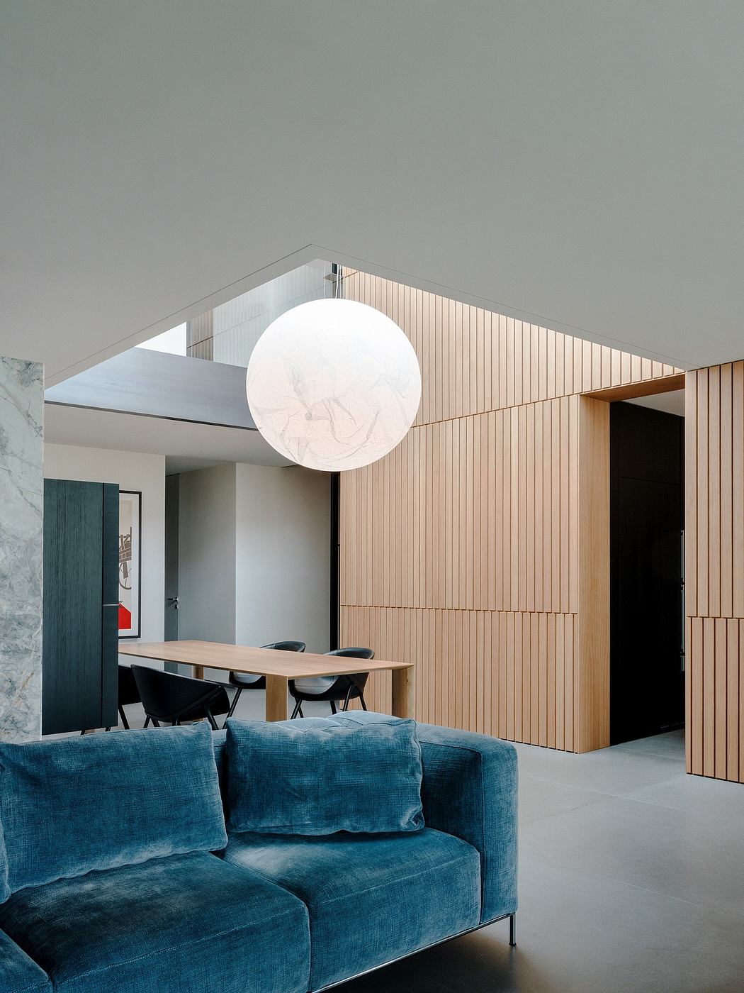 A modern living space with a large white globe light fixture, wood-paneled walls, and a blue velvet sofa.