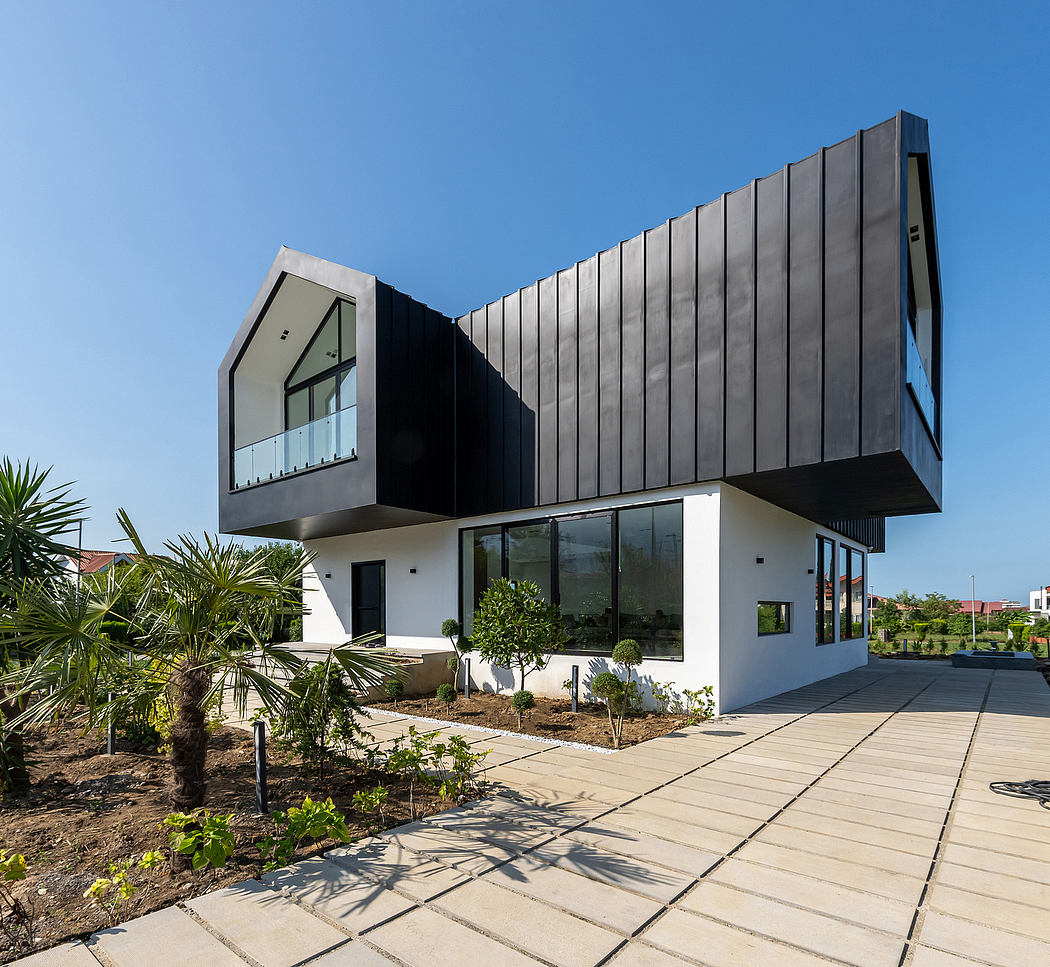 A modern, angular building with a striking black façade and large windows overlooking a garden.
