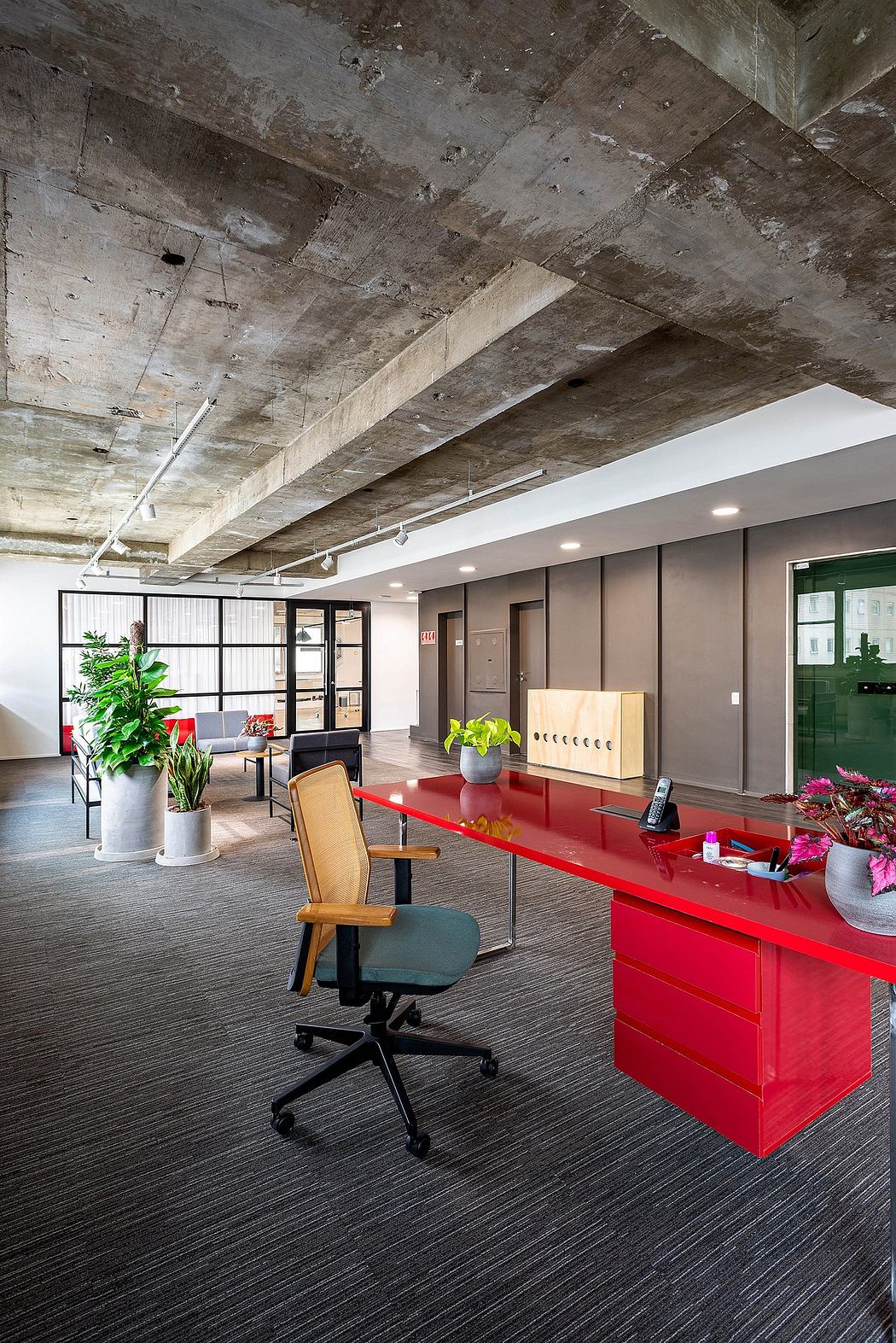 A modern office space with exposed concrete ceilings, minimalist furniture, and vibrant red accents.
