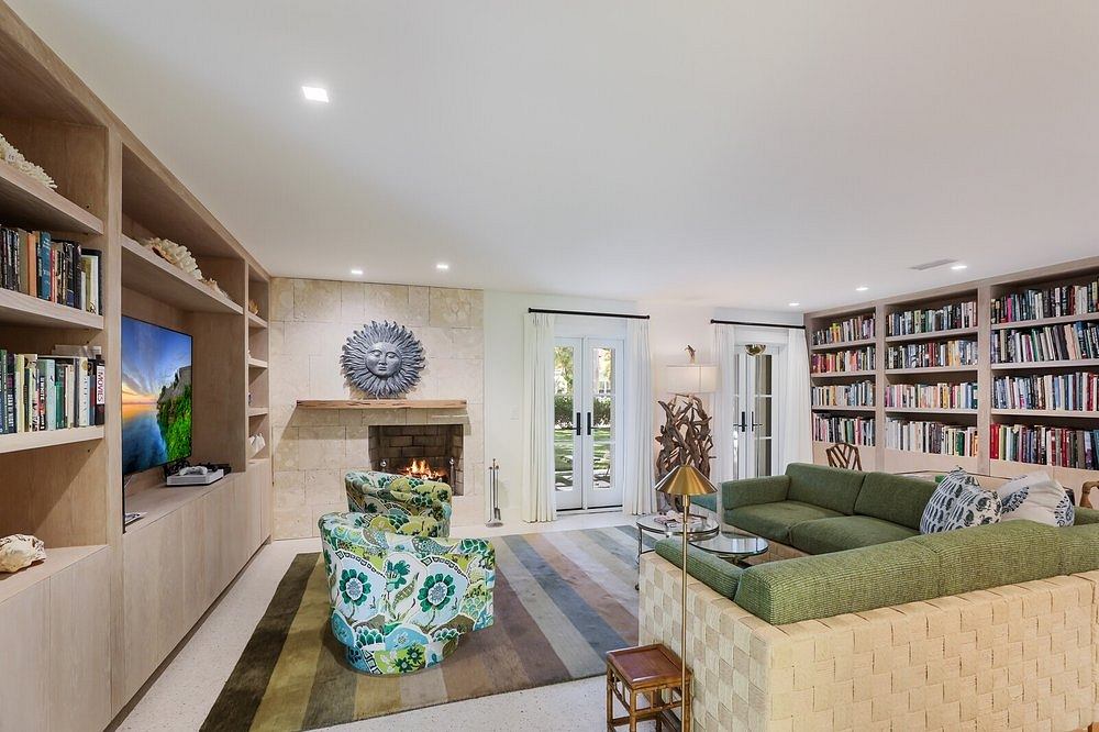 A cozy living room with bookshelves, fireplace, and patterned furniture in warm tones.