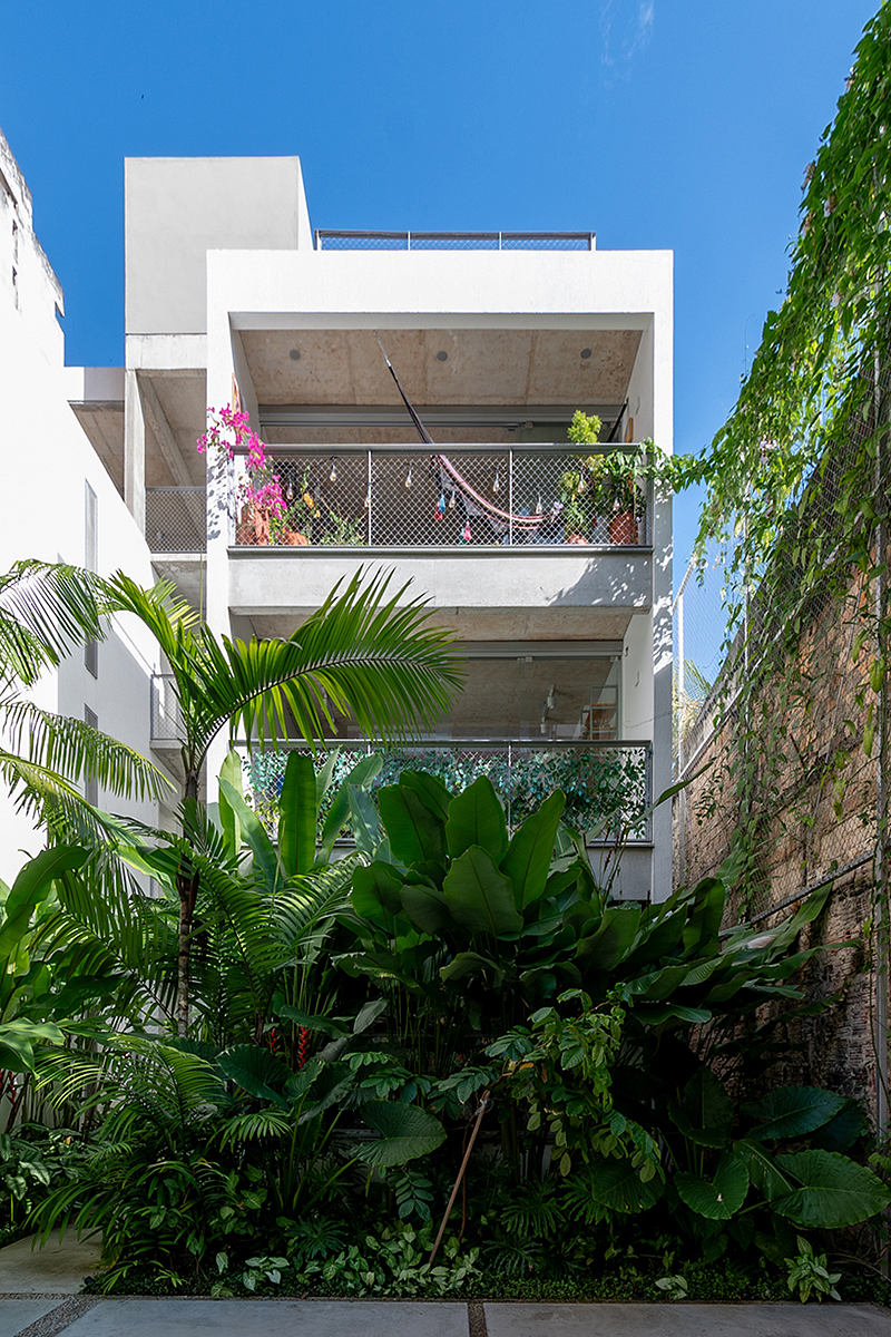 Lush tropical foliage frames a modern multi-story building with balconies and architectural details.