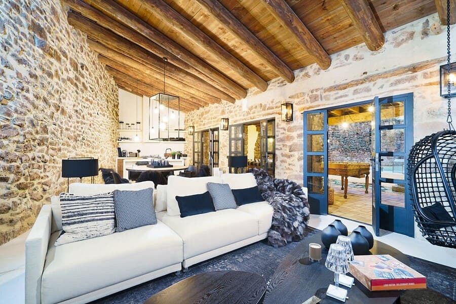 A rustic stone-walled interior featuring exposed wooden beams, plush furnishings, and modern decor elements.