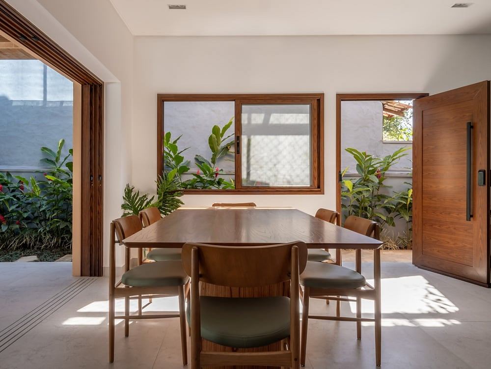 Spacious dining area with wooden furniture, large windows, and lush indoor plants.