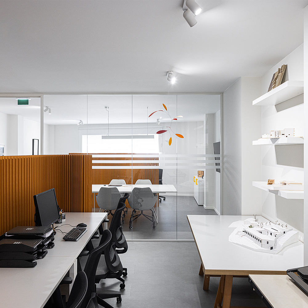 A minimalist, open-concept office space with glass walls, wooden partitions, and modern furnishings.