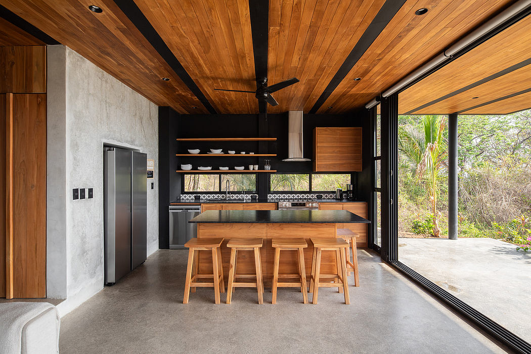 A modern kitchen with wooden ceiling, sleek appliances, and a breakfast bar overlooking nature.