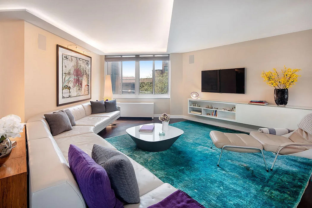 Cozy living room with large gray sectional, colorful rug, wall art, and modern furniture.