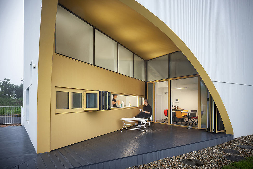 Contemporary architectural design with curved golden facade, expansive windows, and elevated porch.