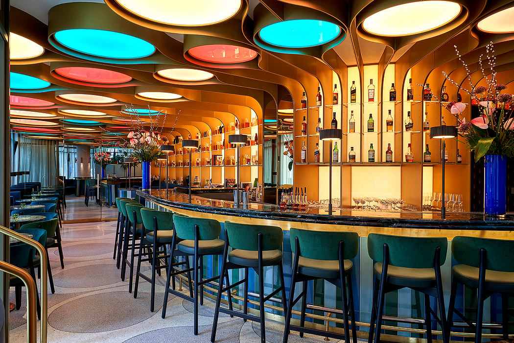 Vibrant color-blocked ceiling, curved bar with bottle display, and plush teal seating.
