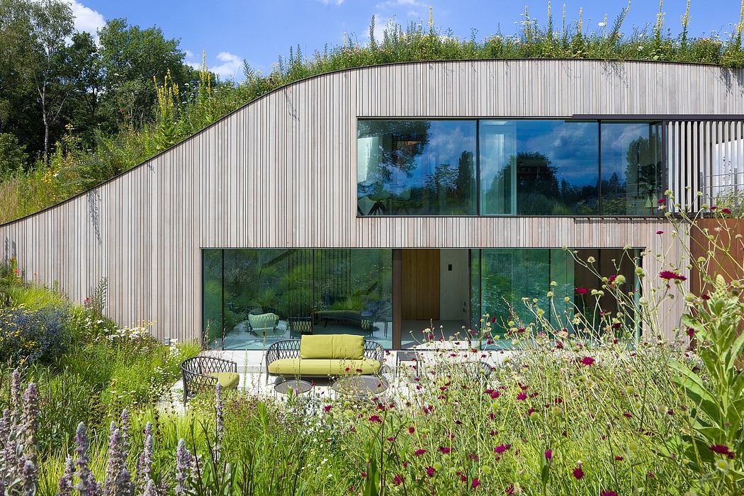 Modern cabin-like structure with glass walls overlooking a lush, colorful garden.