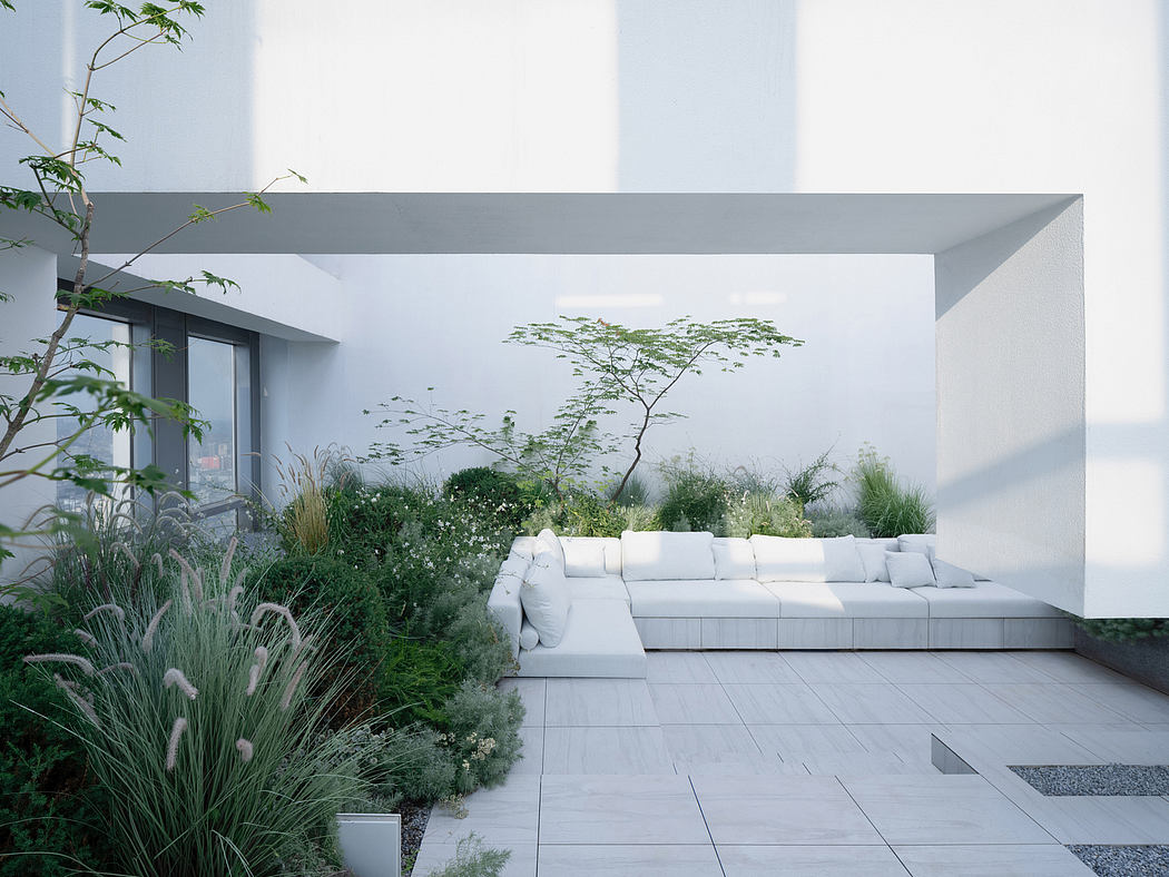 A modern, minimalist outdoor space with a white lounge seating area and lush greenery.