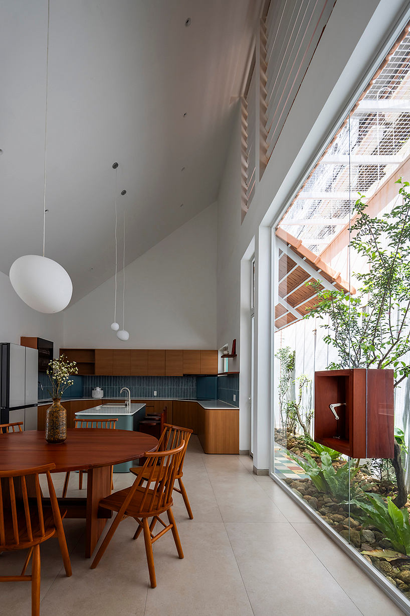 A modern kitchen-dining area with wooden furnishings, high ceilings, and an expansive window overlooking greenery.