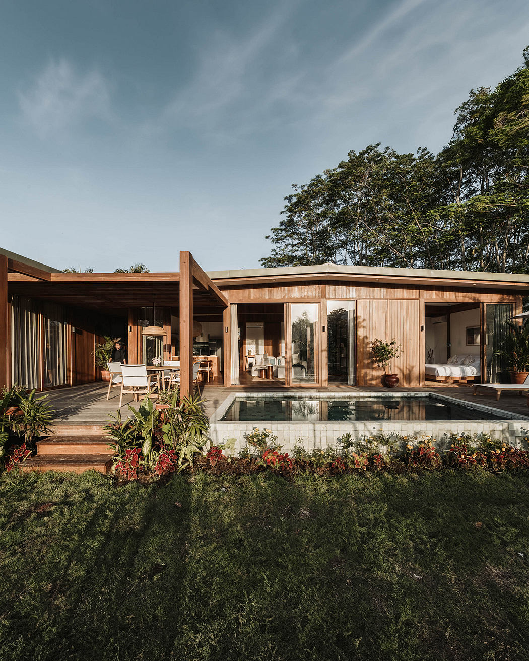 Modern, wood-paneled home with open floor plan, covered patio, and swimming pool surrounded by lush greenery.