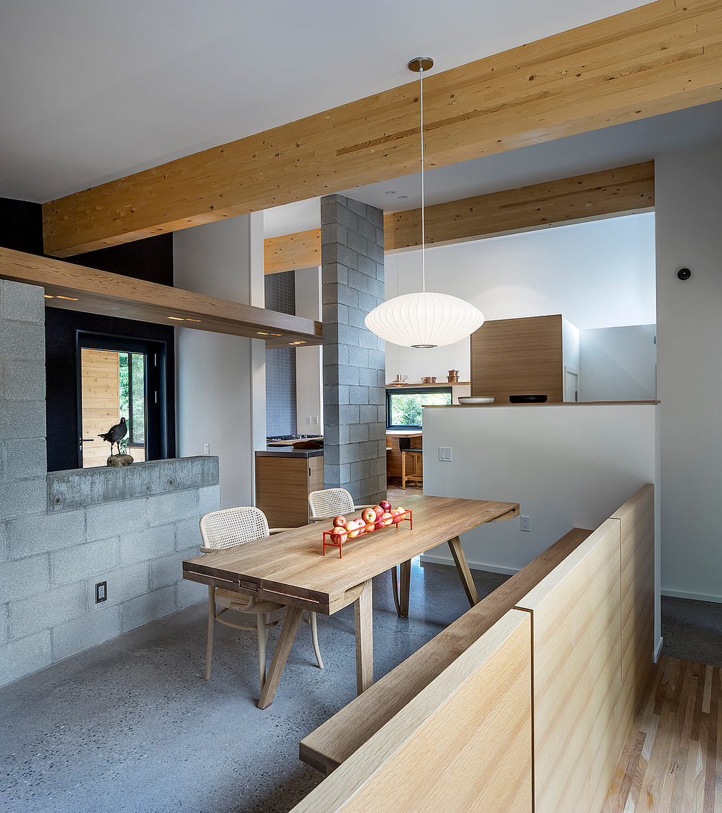 A modern, minimalist kitchen with a wooden dining table, exposed beams, and a concrete fireplace.