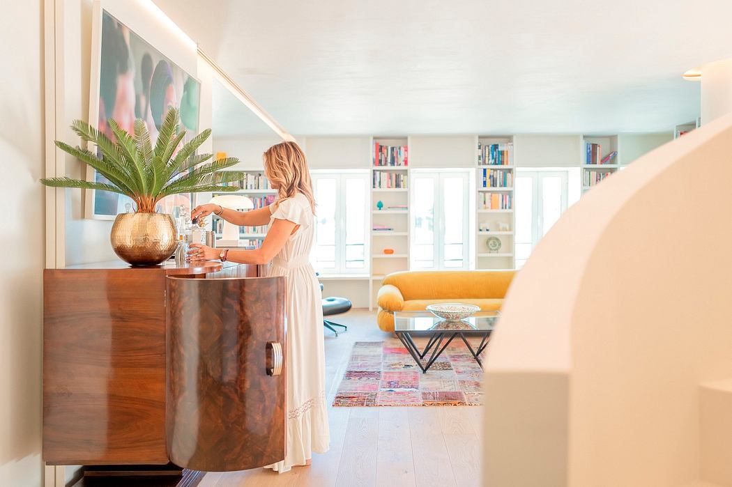 Elegant living room with cozy furnishings, bookshelves, and a woman in a white dress by a wooden cabinet.