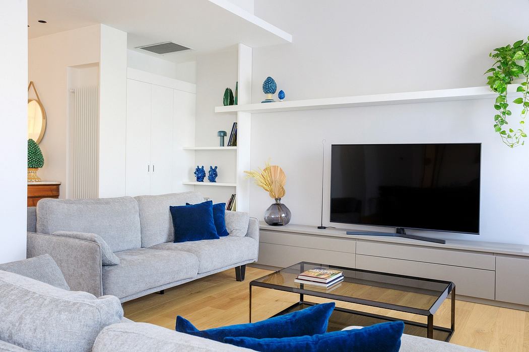 Minimalist living room with gray sofa, wooden coffee table, and geometric shelving displaying decor.