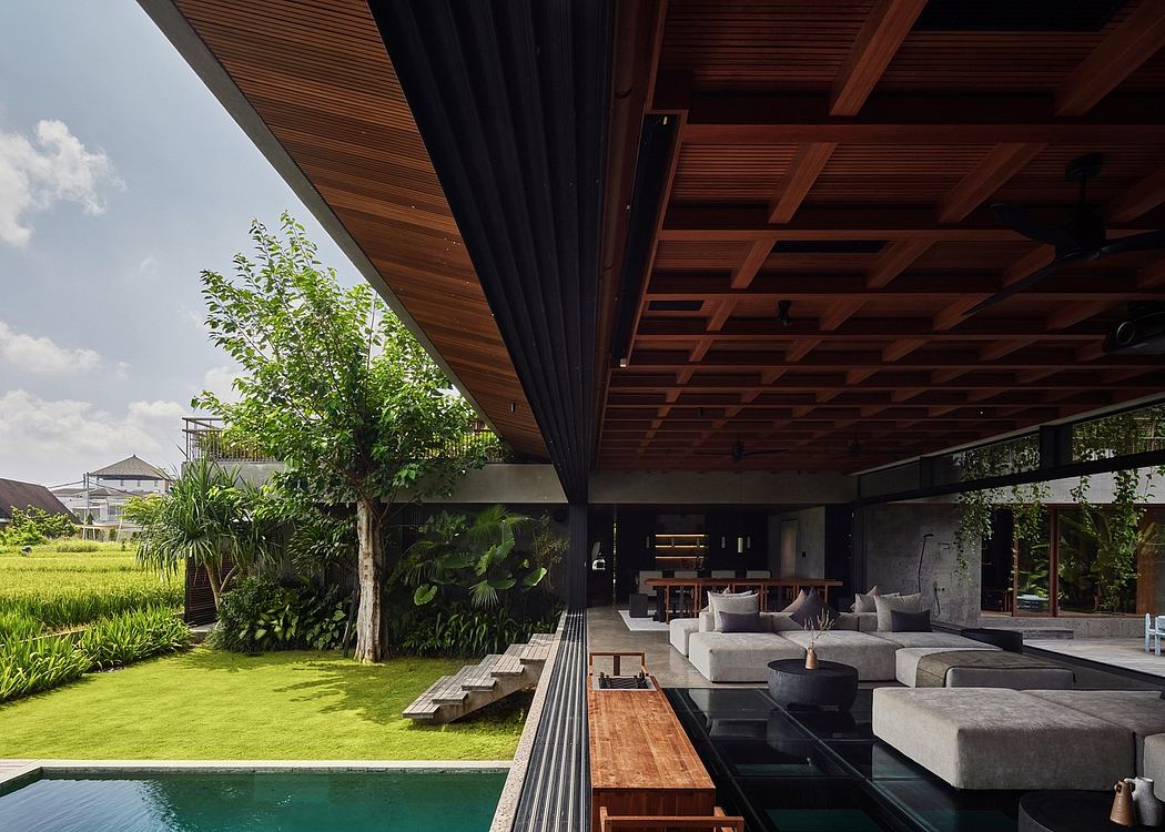 Lush tropical garden visible through the open-air living space with wooden beams and sleek furnishings.
