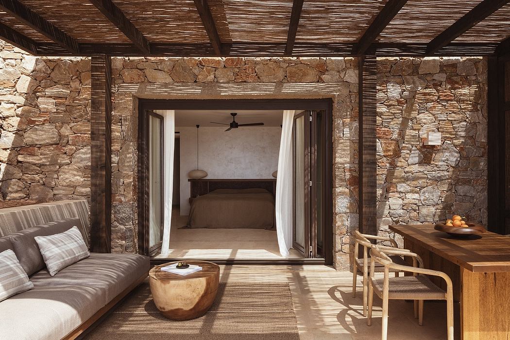 A rustic, stone-walled interior with exposed wooden beams, white curtains, and warm furnishings.