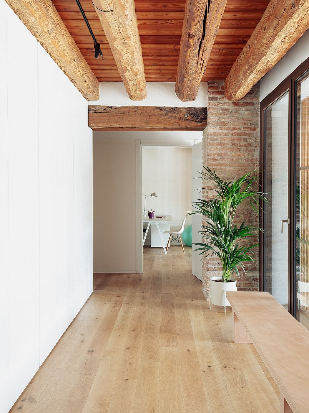 Rustic exposed wooden beams and brick walls, with a minimalist desk and potted plant.