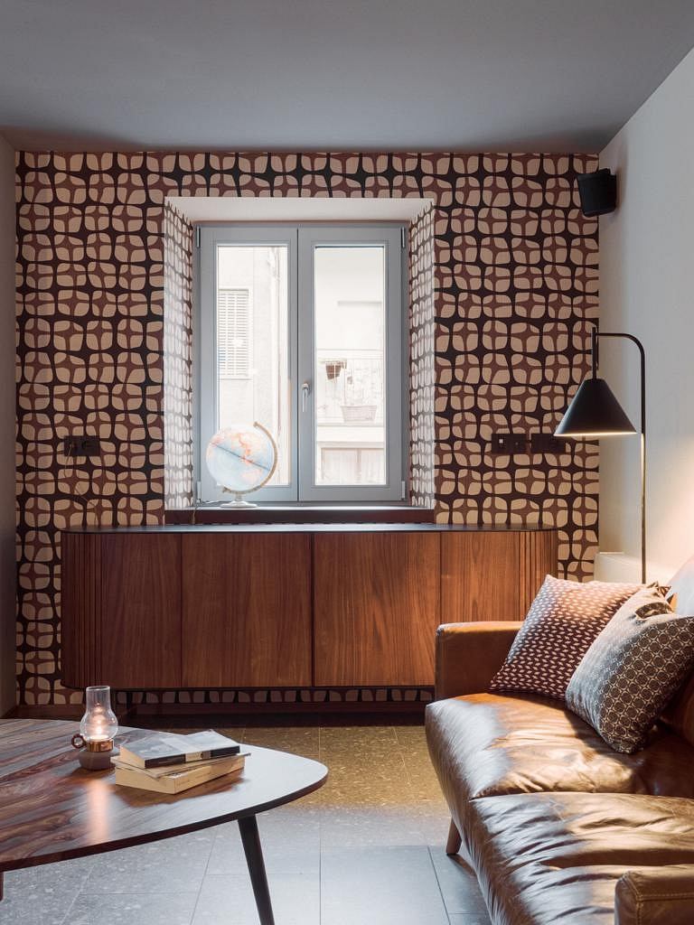 A cozy living room with wooden furniture, patterned wallpaper, and a sleek coffee table.