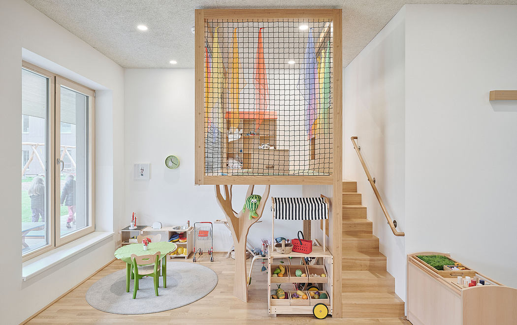 A bright, open play area with wooden structures, shelving, and a colorful climbing net.