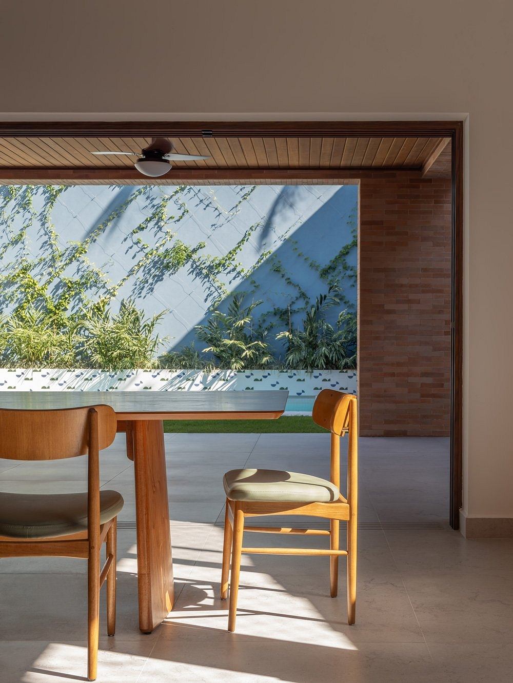 A cozy dining area with wooden furniture, brick walls, and a large window overlooking a lush, verdant landscape.