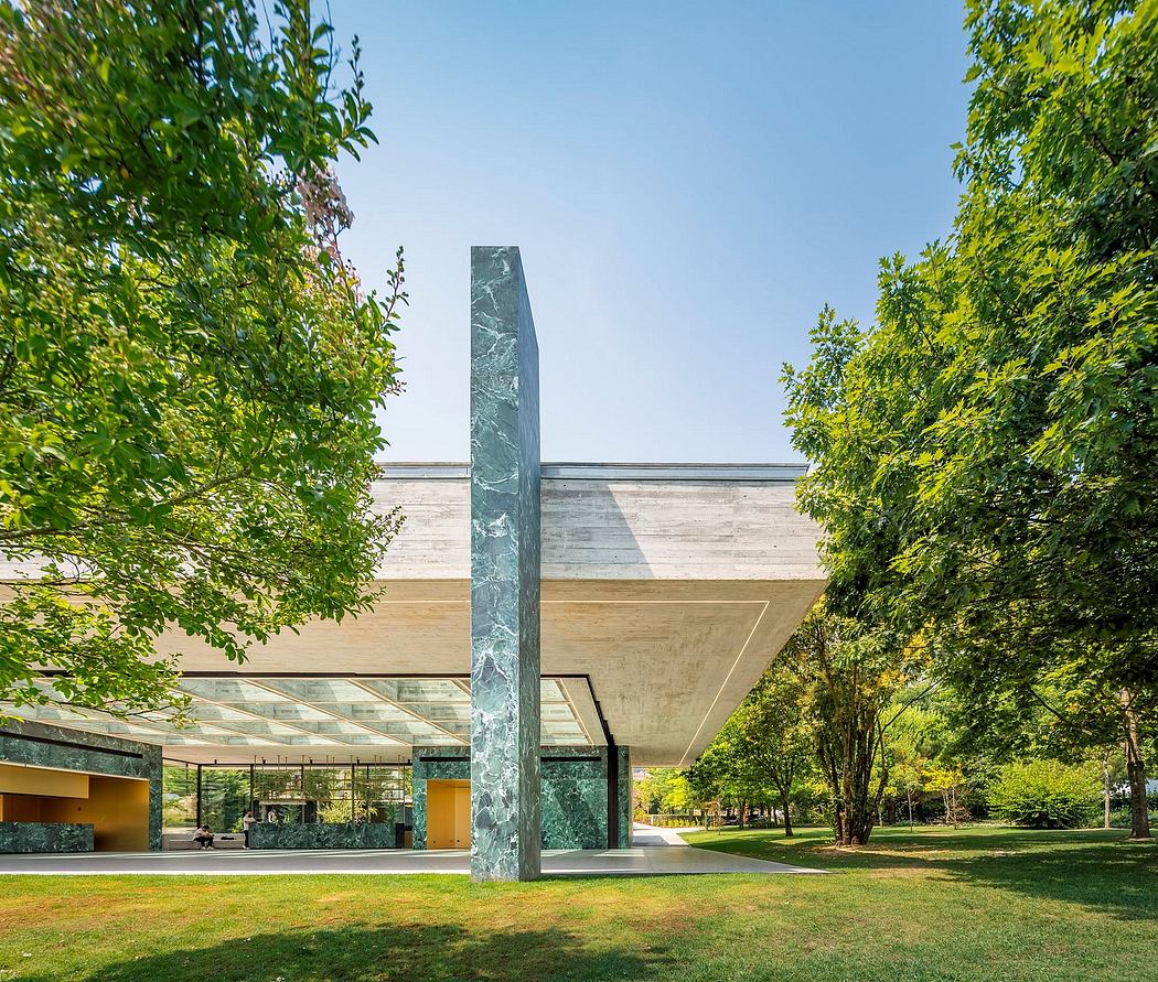 Striking green marble obelisk stands before a modern, glass-paneled structure surrounded by lush greenery.