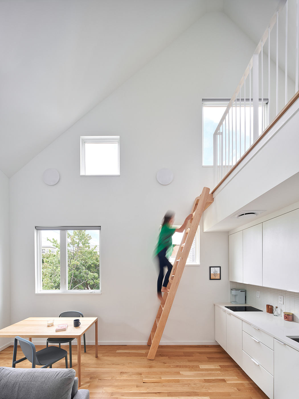 Bright, airy interior with wooden stairs, minimalist kitchen, and views of trees outside.