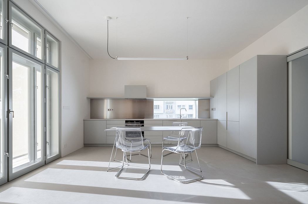 Minimalist kitchen with sleek grey cabinets, stainless steel appliances, and transparent chairs.