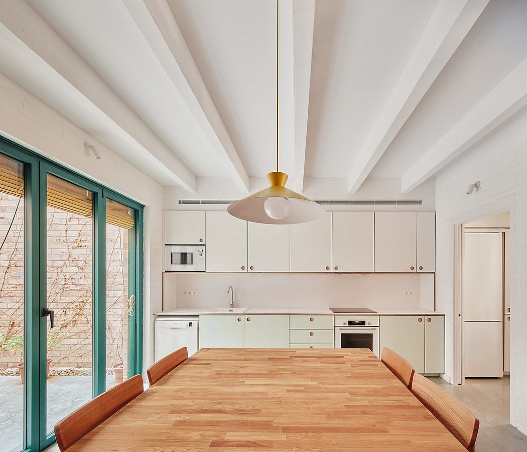Minimalist kitchen and dining area with wooden table, white cabinets, and large windows.