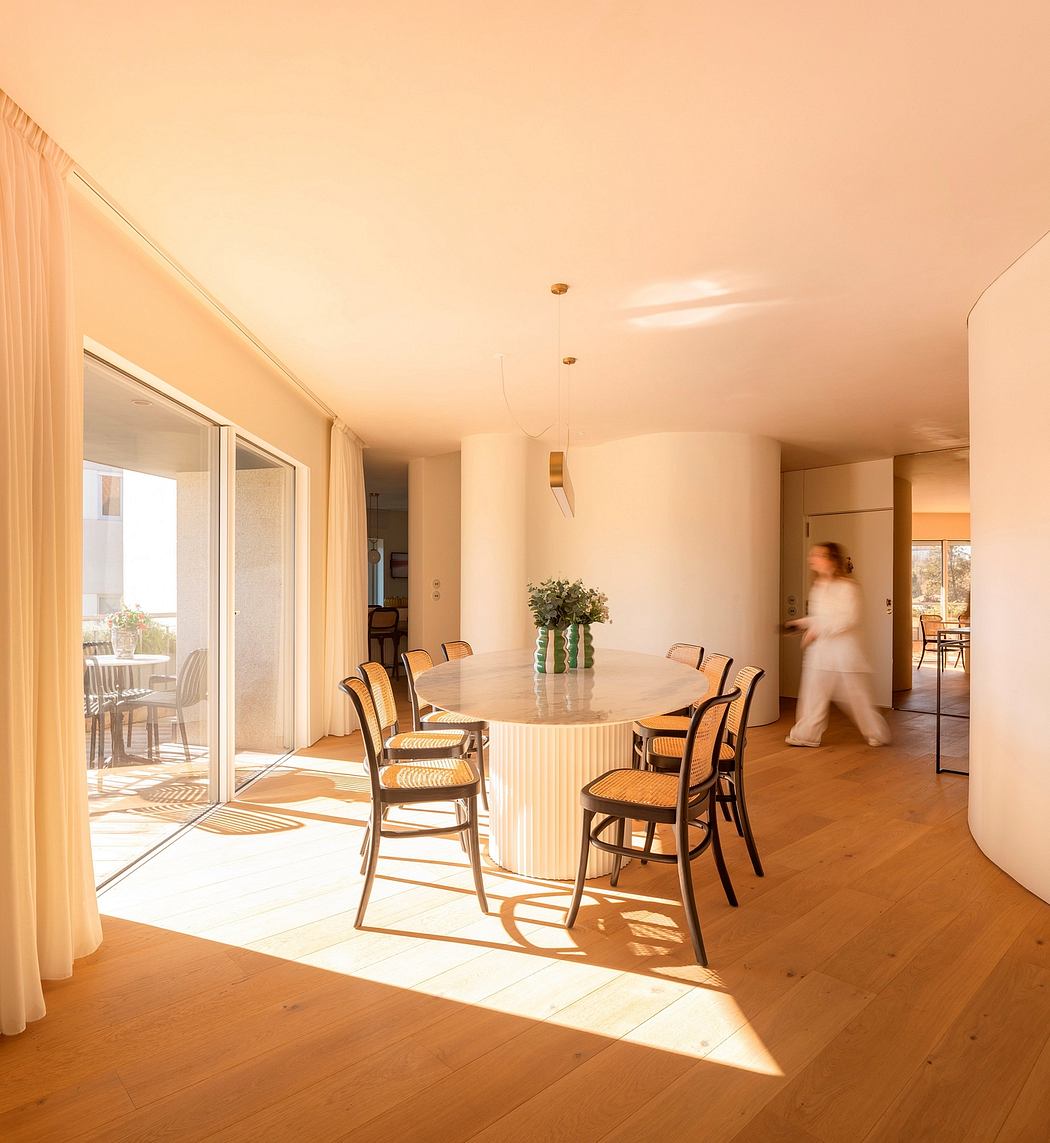 Spacious dining room with a large oval table surrounded by wooden chairs, overlooking a balcony.