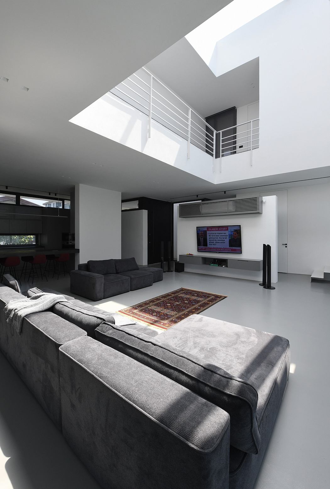 Spacious modern living room with sleek grey furniture, a large TV, and a skylight above.