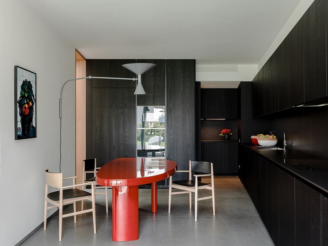 A sleek, modern dining area with a bold red oval table and black wood cabinetry.
