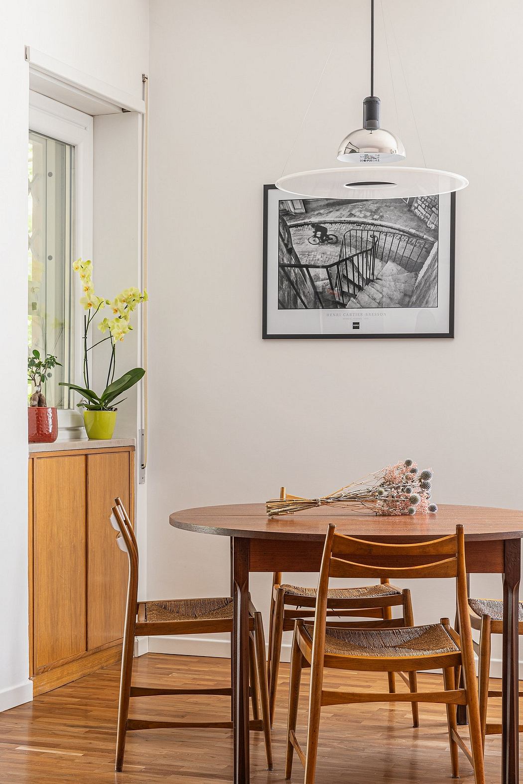 A cozy dining area with a round wood table, woven chairs, and a framed black-and-white photograph.