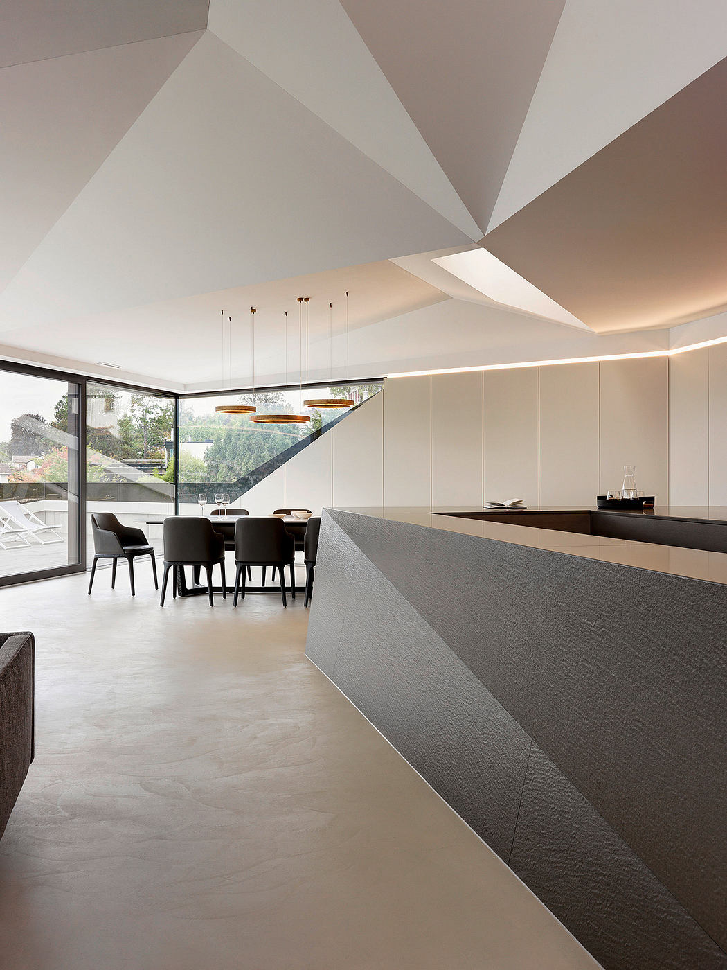 Sleek, modern dining room with angular ceiling, suspended lighting, and large windows.