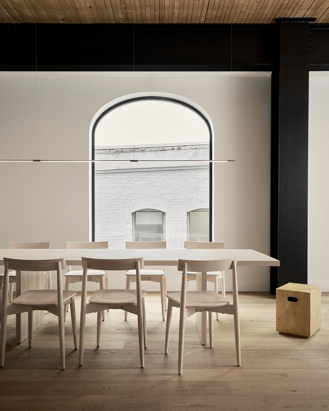 A minimalist dining room with a curved arched window, wooden chairs, and simple decor.