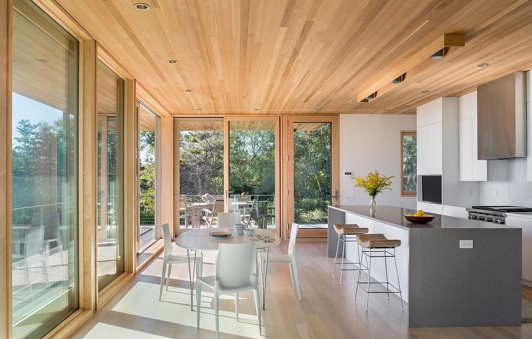 Bright, expansive open-plan kitchen and dining area with wood-paneled ceilings and large windows.