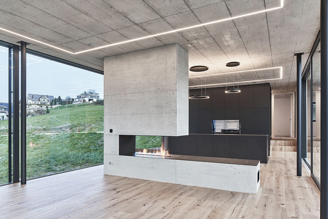 Minimalist concrete interior with large windows, wood floors, and sleek black kitchen.