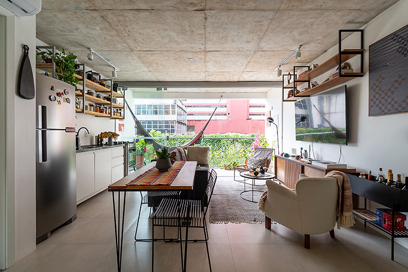 Modern open-plan living area with concrete ceiling, wooden dining table, and shelving units.