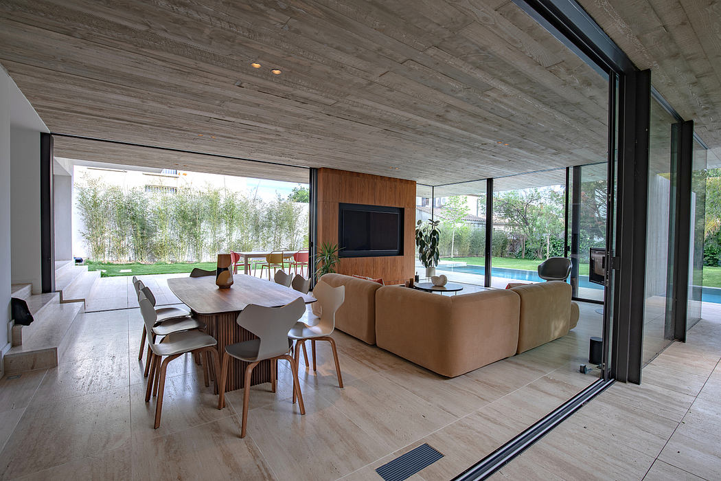 Spacious, modern living area with wood-paneled ceiling, large glass windows overlooking lush greenery.