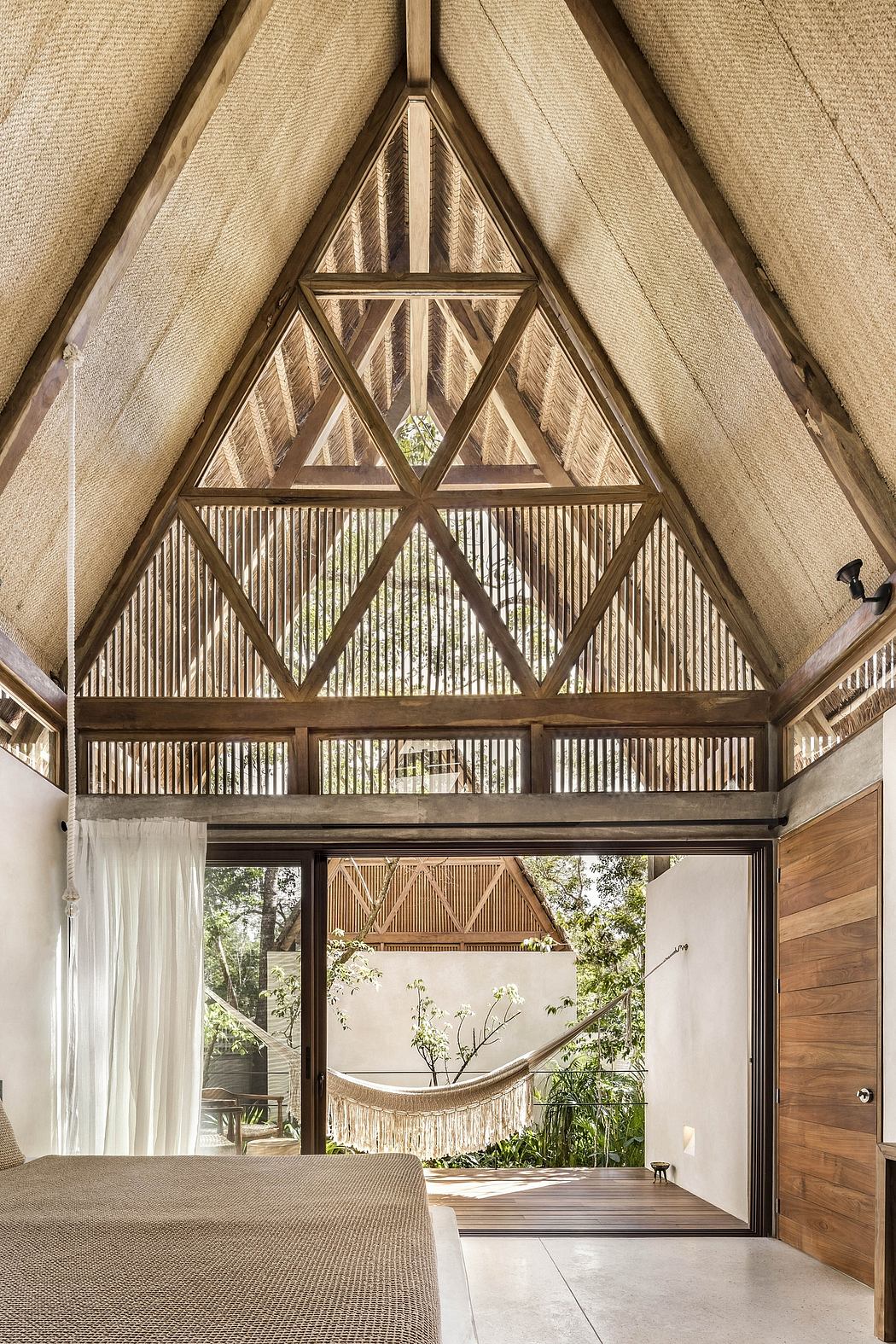 Rustic A-frame structure with intricate wooden beams, framing a hammock and lush outdoor view.
