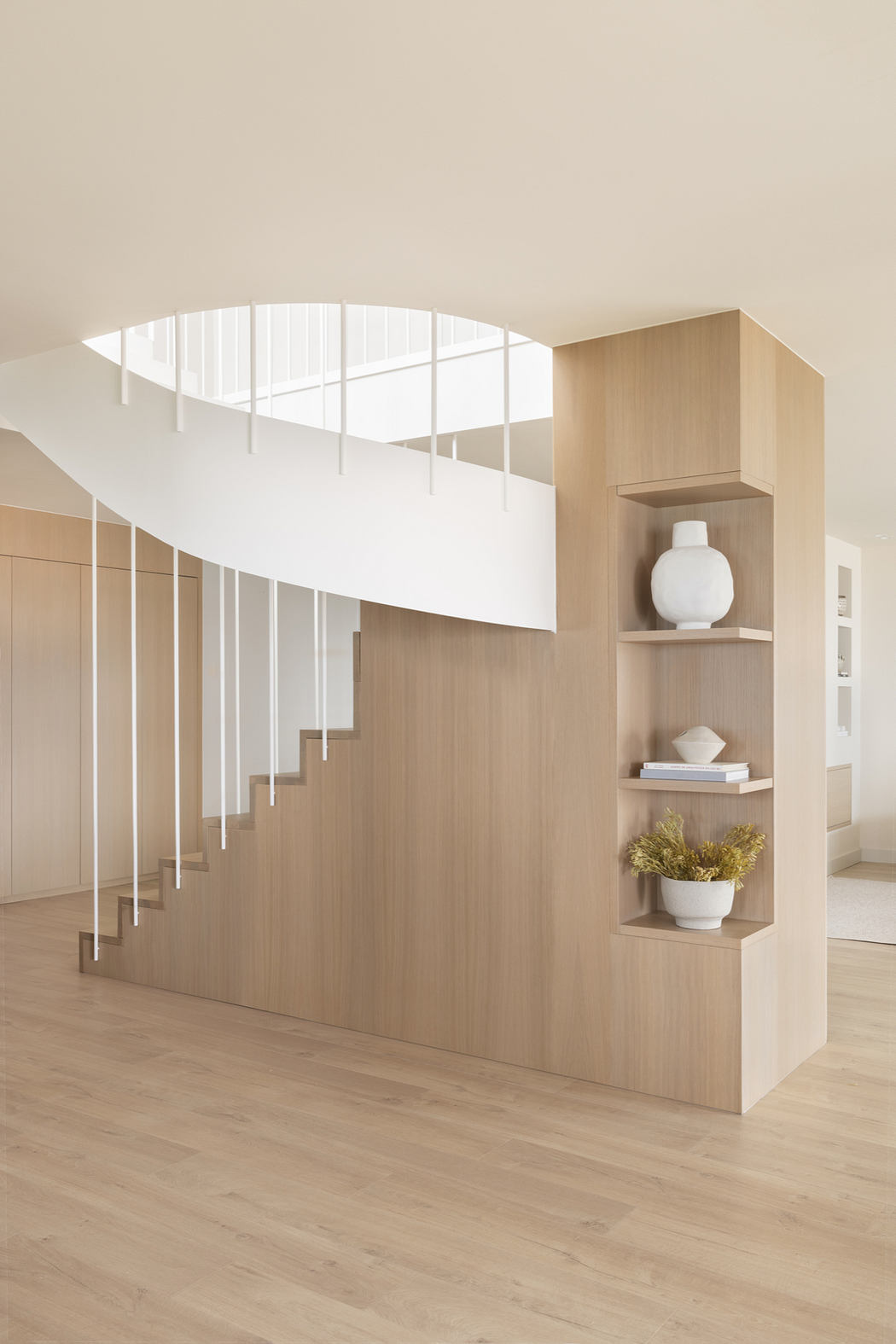 Modern minimalist interior with a curved staircase, built-in shelving, and natural light.