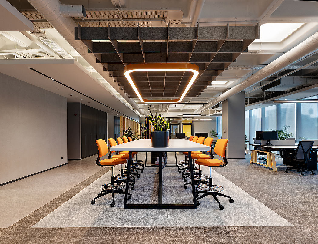Modern office space with geometric lighting fixture, orange chairs, and open layout.