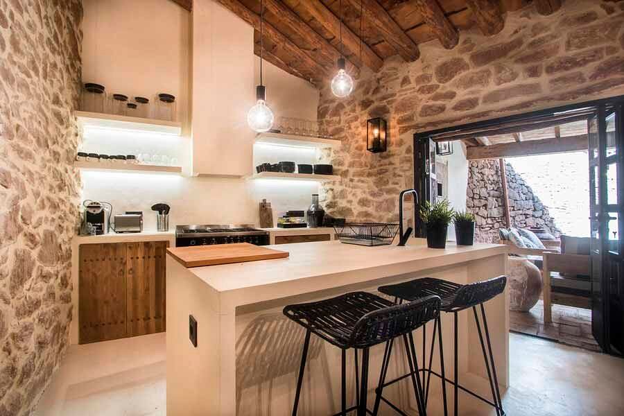 Rustic kitchen with stone walls, wooden beams, and modern fixtures and furnishings.