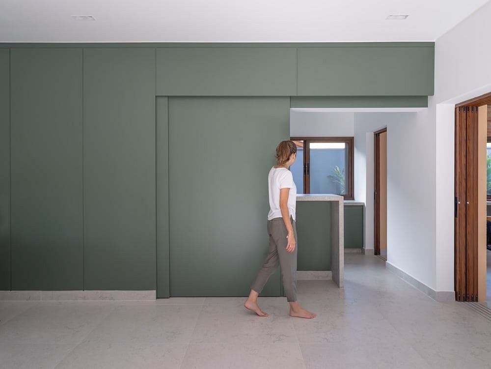 Modern minimalist interior with a person walking through a room with green paneled walls and wooden doors.