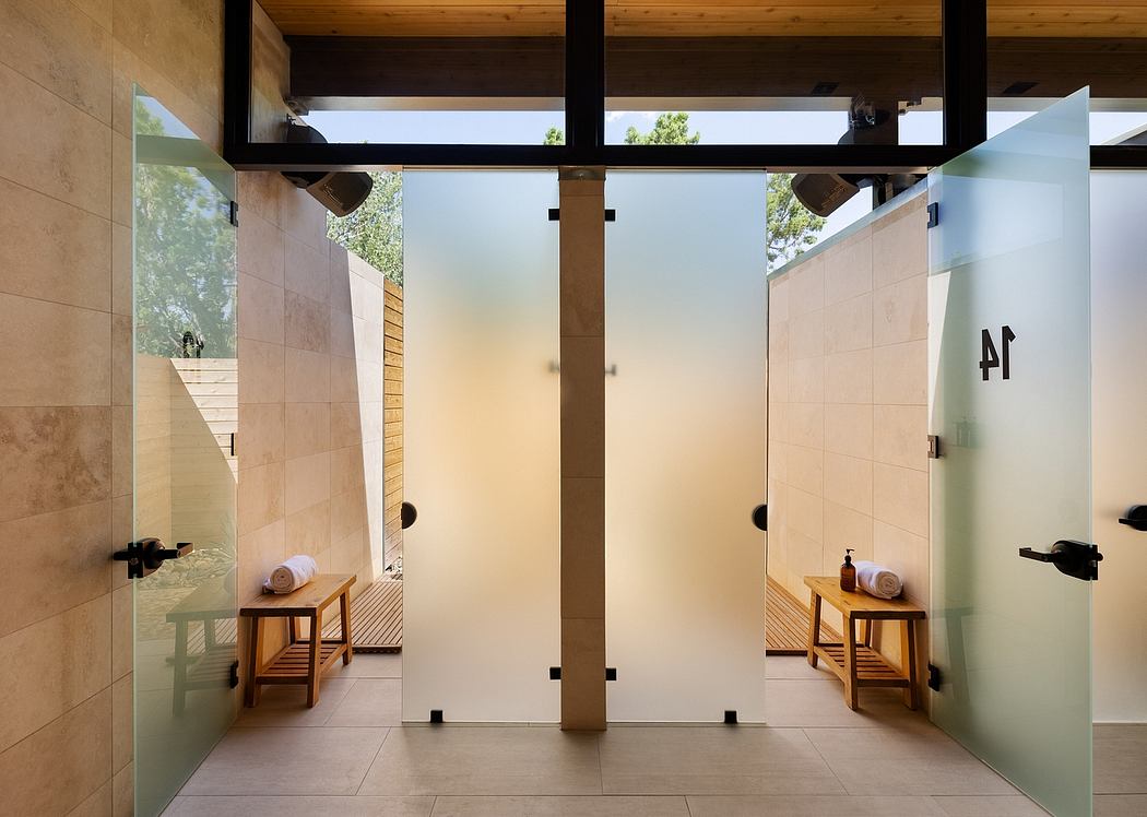 A modern, minimalist bathroom design with glass shower stalls, tiled walls, and wooden benches.