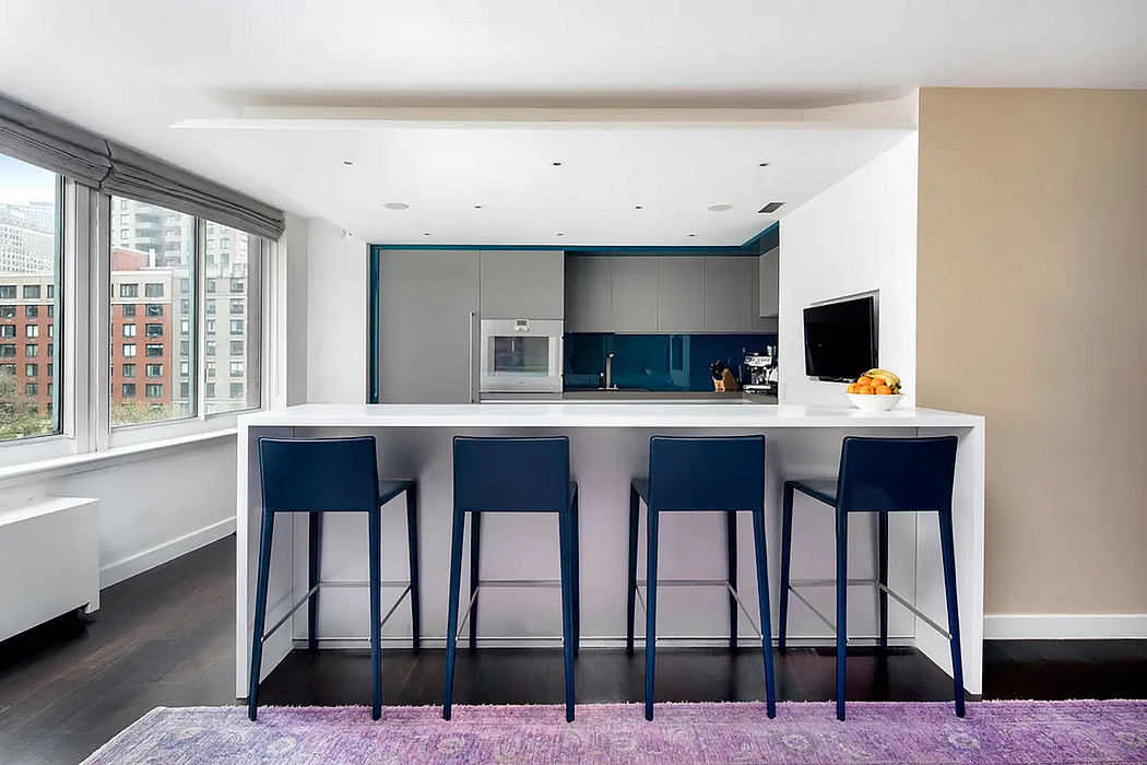 Sleek modern kitchen with gray cabinetry, bar seating, and large windows overlooking cityscape.